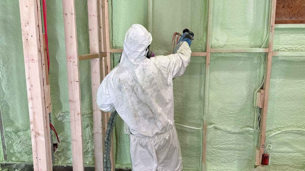 Team member of C&K Fibertech dressed in protective suit and installation spray foam insulation in wall.